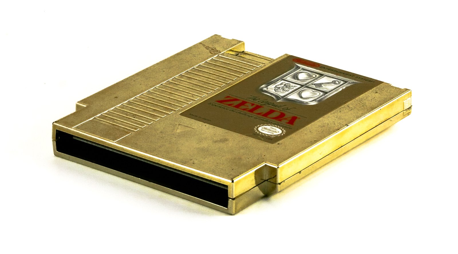 The gold-coloured cartridge of the 1986 Nintendo game The Legend of Zelda, photographed on white, its label showing a silver shield crest and the red word ZELDA.