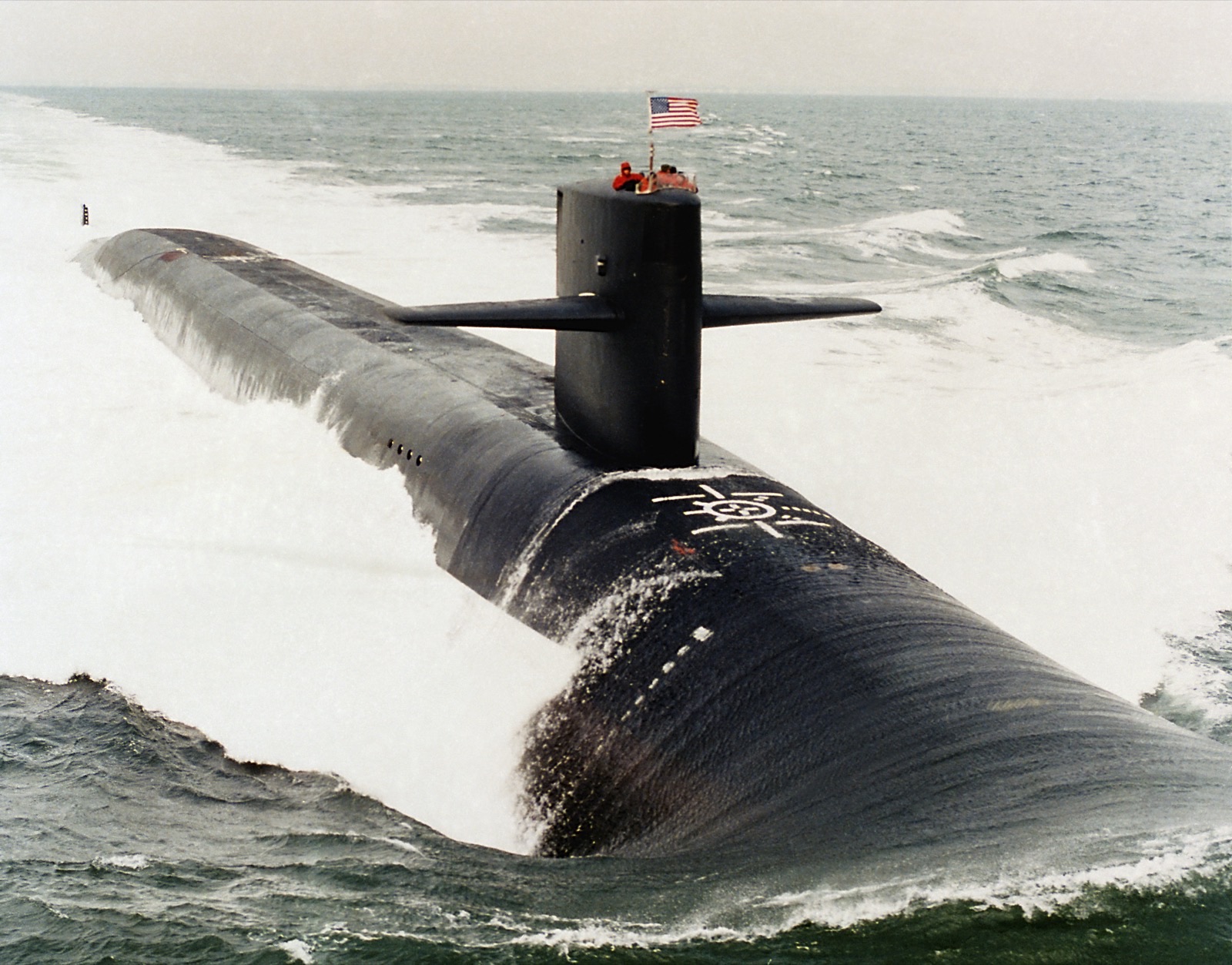 USS Georgia cuts through the water, with its bow, sail and wake visible.